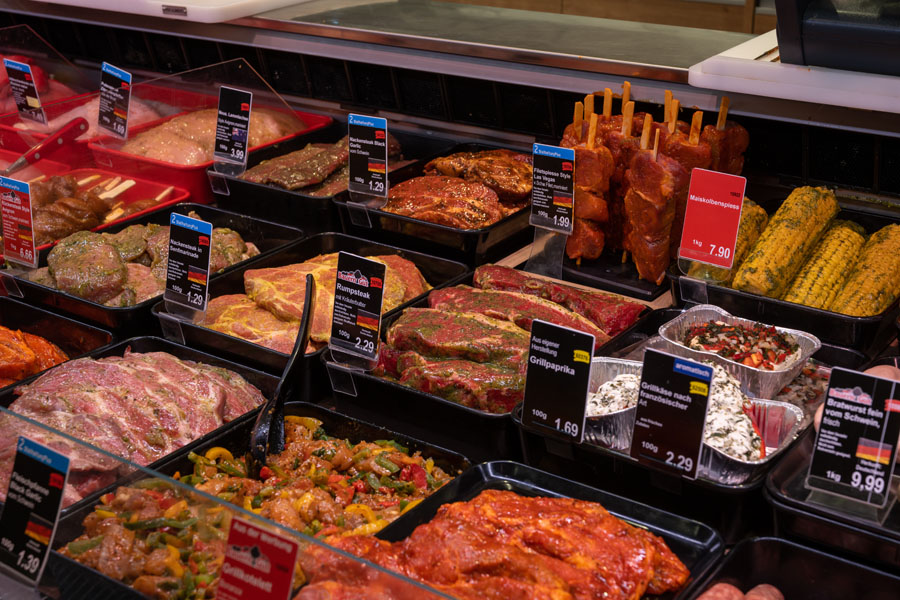 Frische Fleischtheke in einem Supermarkt mit verschiedenen marinierten Grillfleisch-Spezialitäten und Beilagen