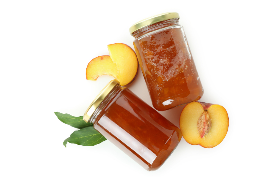 Pfirsichmarmelade in Gläsern mit frischen Pfirsichhälften und Blättern.